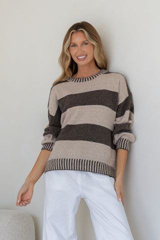 Woman wearing a beige and brown striped knit sweater and white pants