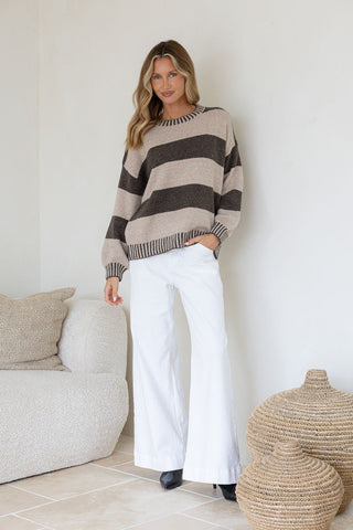 Woman wearing a striped beige and brown knit sweatshirt with white wide-leg pants.