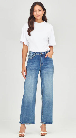 Woman wearing a white short-sleeve t-shirt and wide-leg blue jeans with white sandals.