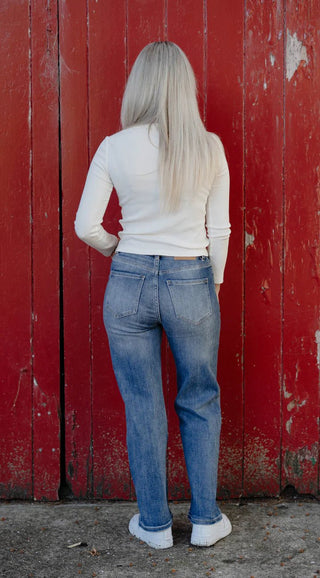 Woman with long blonde hair wearing a white long-sleeve top and blue straight-leg jeans.