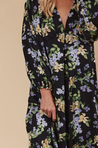 Woman wearing a black long-sleeved dress with a purple and yellow floral print.