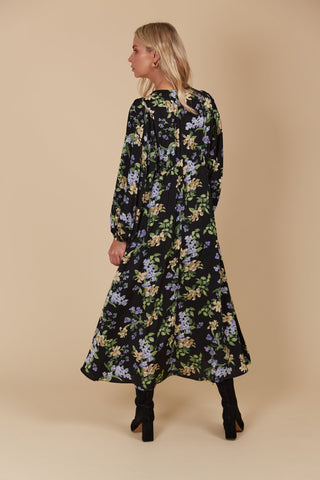 Woman wearing a long-sleeved black floral maxi dress and black boots, viewed from behind.