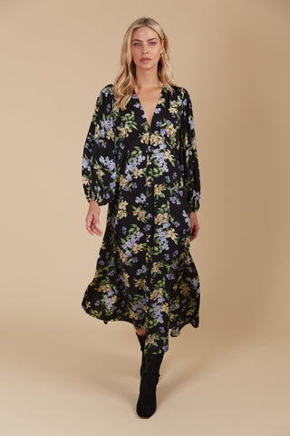 Woman wearing a black floral maxi dress with long puff sleeves and black boots.
