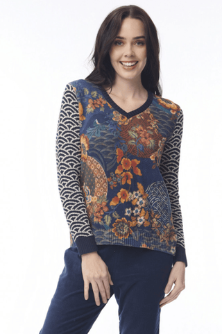 Woman wearing a floral print v-neck sweater with patterned navy sleeves and blue pants.