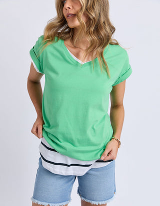 Woman wearing a green V-neck t-shirt over a white striped top and denim shorts.