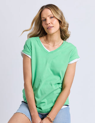 Woman wearing a green v-neck t-shirt and denim shorts against a white background.