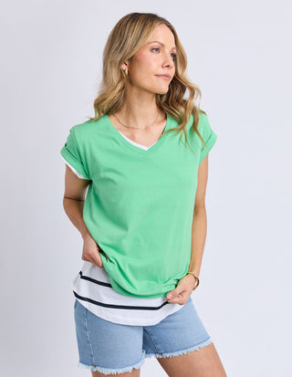 Woman wearing a green v-neck t-shirt layered over a white striped top and denim shorts.