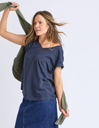 Woman wearing a navy blue t-shirt and denim skirt holding an olive green garment.