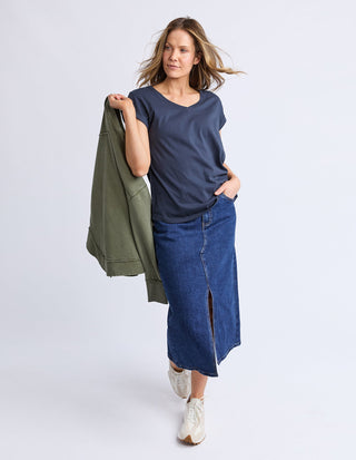 Woman wearing a navy v-neck t-shirt, long blue denim skirt, and white sneakers.