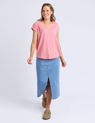 Woman wearing a pink short-sleeve t-shirt and a blue denim midi skirt with a front slit.