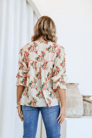 Woman wearing a cream floral print blouse with ruffled sleeves and blue jeans.