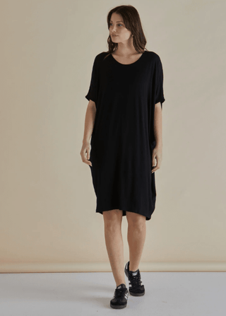 Woman wearing a relaxed fit black short sleeve t-shirt dress and black sneakers.