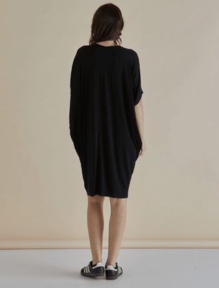Rear view of a woman wearing a loose-fitting black short-sleeved dress and sneakers.