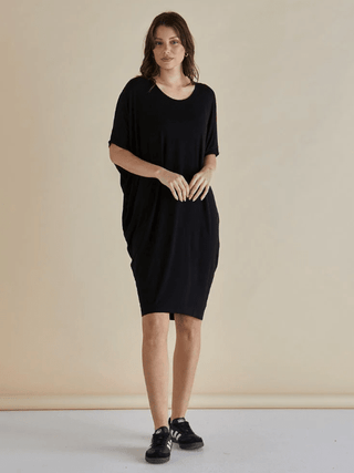 Woman wearing a black short sleeve oversized t-shirt dress and black sneakers.