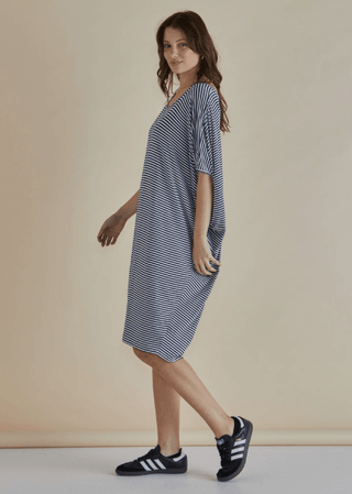 Woman wearing a navy and white striped t-shirt dress and black sneakers.