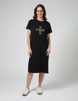Woman wearing a black t-shirt dress with a green floral cross print and white sneakers.