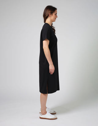 Woman wearing a black short-sleeved midi dress and white sneakers.