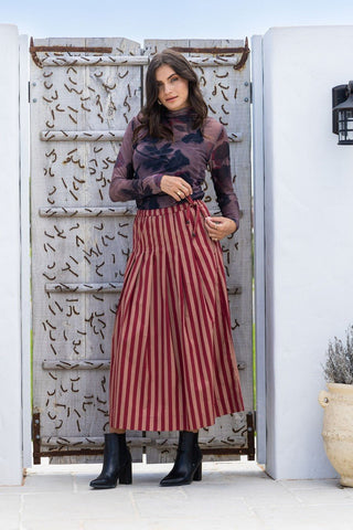 Woman wearing a purple tie-dye mesh top and red striped pleated midi skirt.