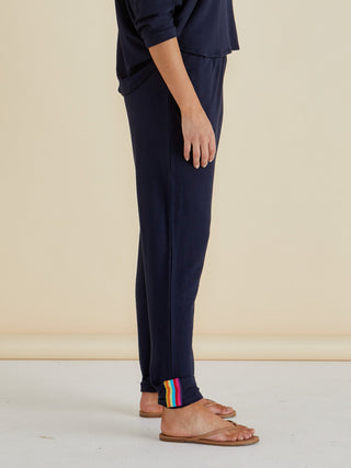 Woman wearing navy blue leisure wear lounge pants with rainbow stripe detail at the ankle.
