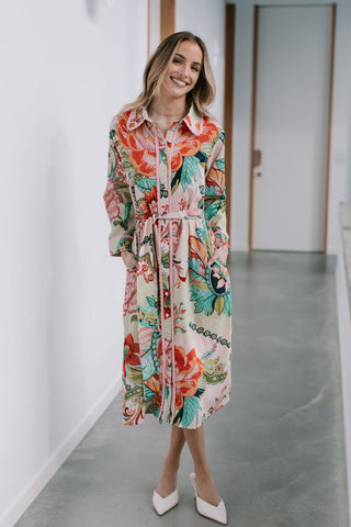 Woman wearing a long-sleeved floral print midi dress with a waist tie and white heels
