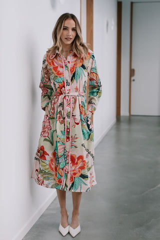 Woman wearing a long-sleeved floral print midi dress with a belted waist and white heels.