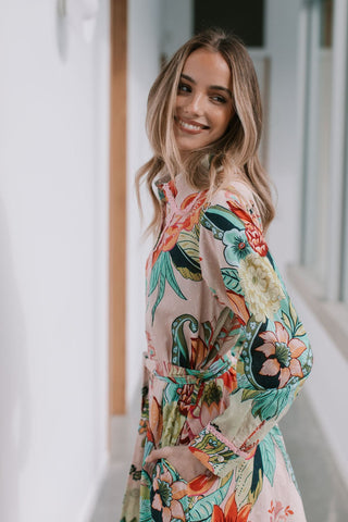 Woman wearing a pink floral print dress with long sleeves and a tie waist