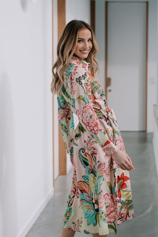 Woman wearing a long-sleeved floral print midi dress in pink and green tones.