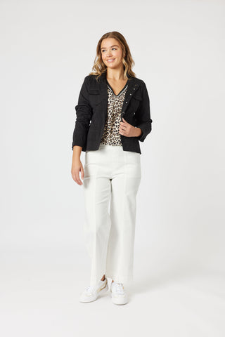 Woman wearing a black jacket, leopard print top, and white wide-leg pants with white sneakers.