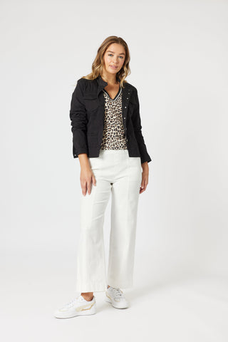 Woman wearing a black jacket, leopard print top, and white wide-leg pants.