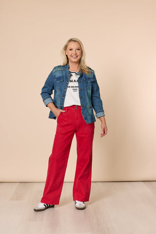 Woman wearing a denim jacket, white graphic tee, and red wide-leg pants.