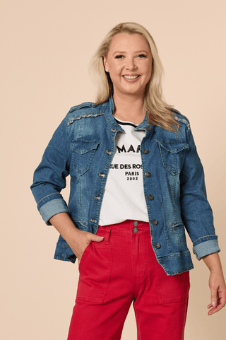 Woman smiling in a blue denim jacket, white graphic t-shirt, and bright red trousers.