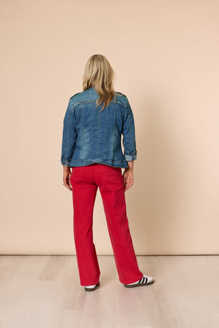 Back view of a woman wearing a blue denim jacket and red flare pants.