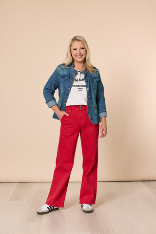 Woman wearing a denim jacket, white graphic tee, and red wide-leg trousers.