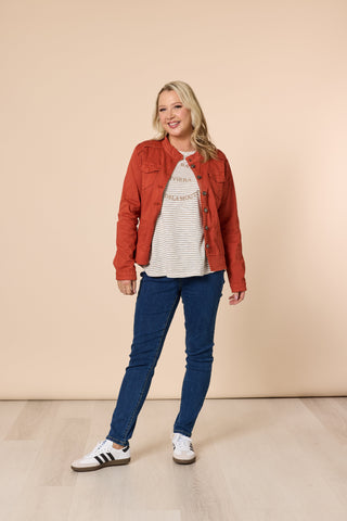 Woman wearing a rust-colored denim jacket, striped t-shirt, and blue skinny jeans.