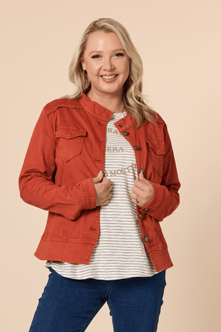Woman wearing a burnt orange denim jacket over a striped t-shirt and blue jeans.