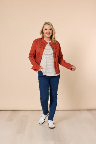 Woman wearing a burnt orange jacket, striped t-shirt, blue jeans, and white sneakers.