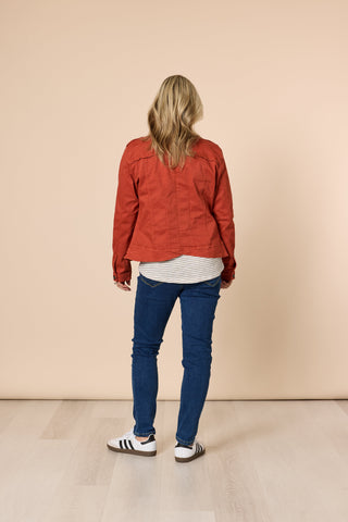 Rear view of a woman wearing a rust-colored denim jacket, striped top, and blue jeans.