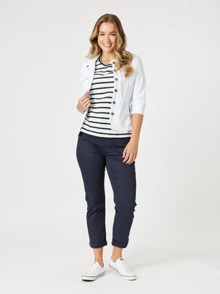 Woman wearing a white denim jacket, navy and white striped t-shirt, and navy cropped pants.