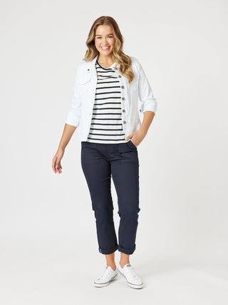 Woman wearing a white denim jacket, navy striped t-shirt, and navy cropped pants.