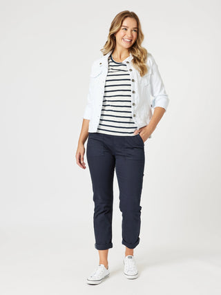 Woman wearing a white denim jacket, navy striped t-shirt, and navy trousers with white sneakers.
