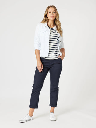 Woman wearing a white denim jacket, striped t-shirt, and navy blue cropped pants with white sneakers.