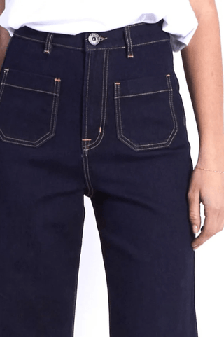 Dark wash denim pants with contrast orange stitching and front patch pockets.