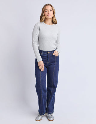 Woman wearing a grey long sleeve sweatshirt and dark blue wide leg denim pants with silver sneakers