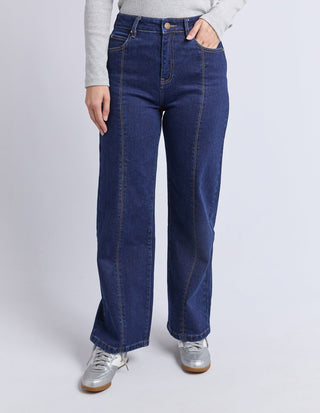 Woman wearing dark blue wide leg denim jeans and silver sneakers.