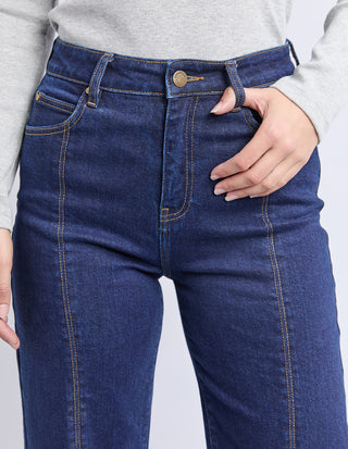 Close-up of a woman wearing high-waisted dark blue denim jeans with orange stitching.