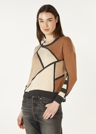 Woman wearing a geometric pattern knit sweater in tan, cream, and black with grey jeans.