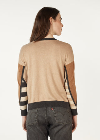 Woman wearing a tan and brown patterned knit sweater and dark denim jeans.