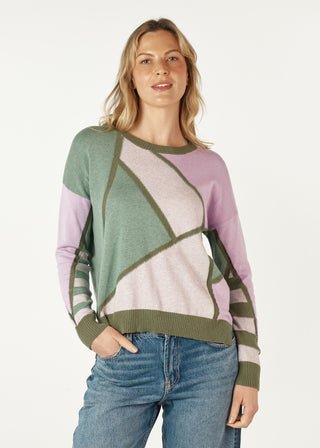 Woman wearing a multi-color geometric pattern knit sweater in sage green and lilac with denim jeans.