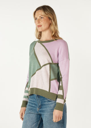 Woman wearing a pastel pink and green colorblock knit sweatshirt with blue jeans.