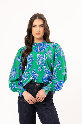 Woman wearing a green floral print long sleeve blouse and dark blue jeans